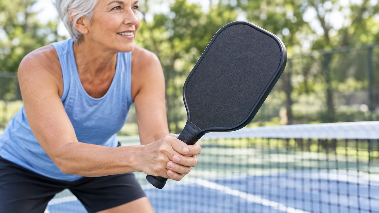 A close view of a player's hand gripping a paddle handle near the net on a sunny court.