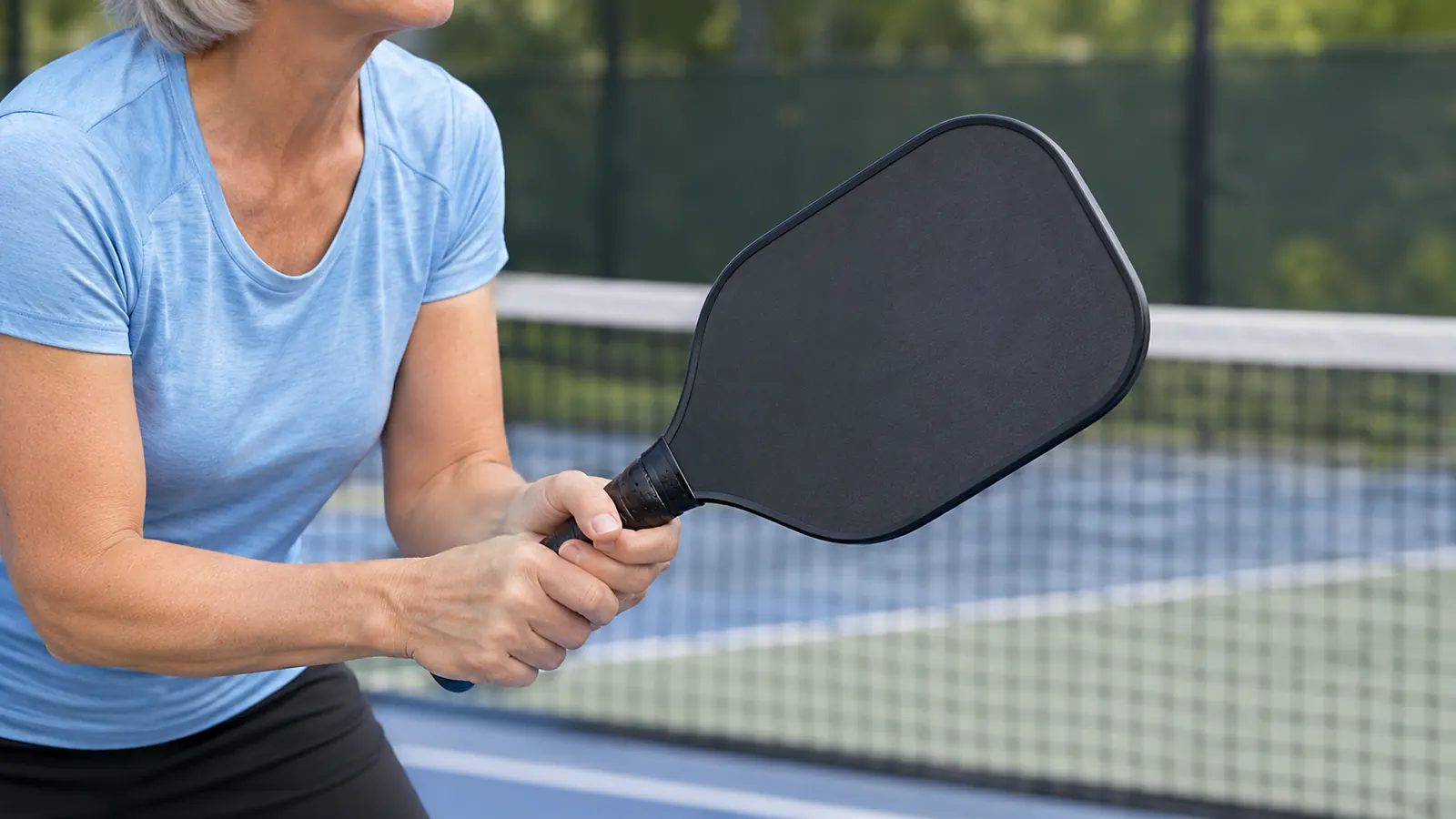 Close view of a player's hands gripping a carbon fiber pickleball paddle at the ready position.