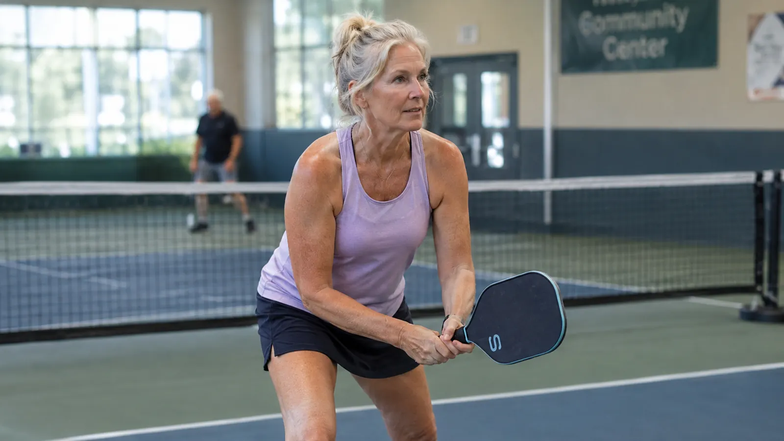 Woman in her sixties at the kitchen line, paddle ready, on an indoor court