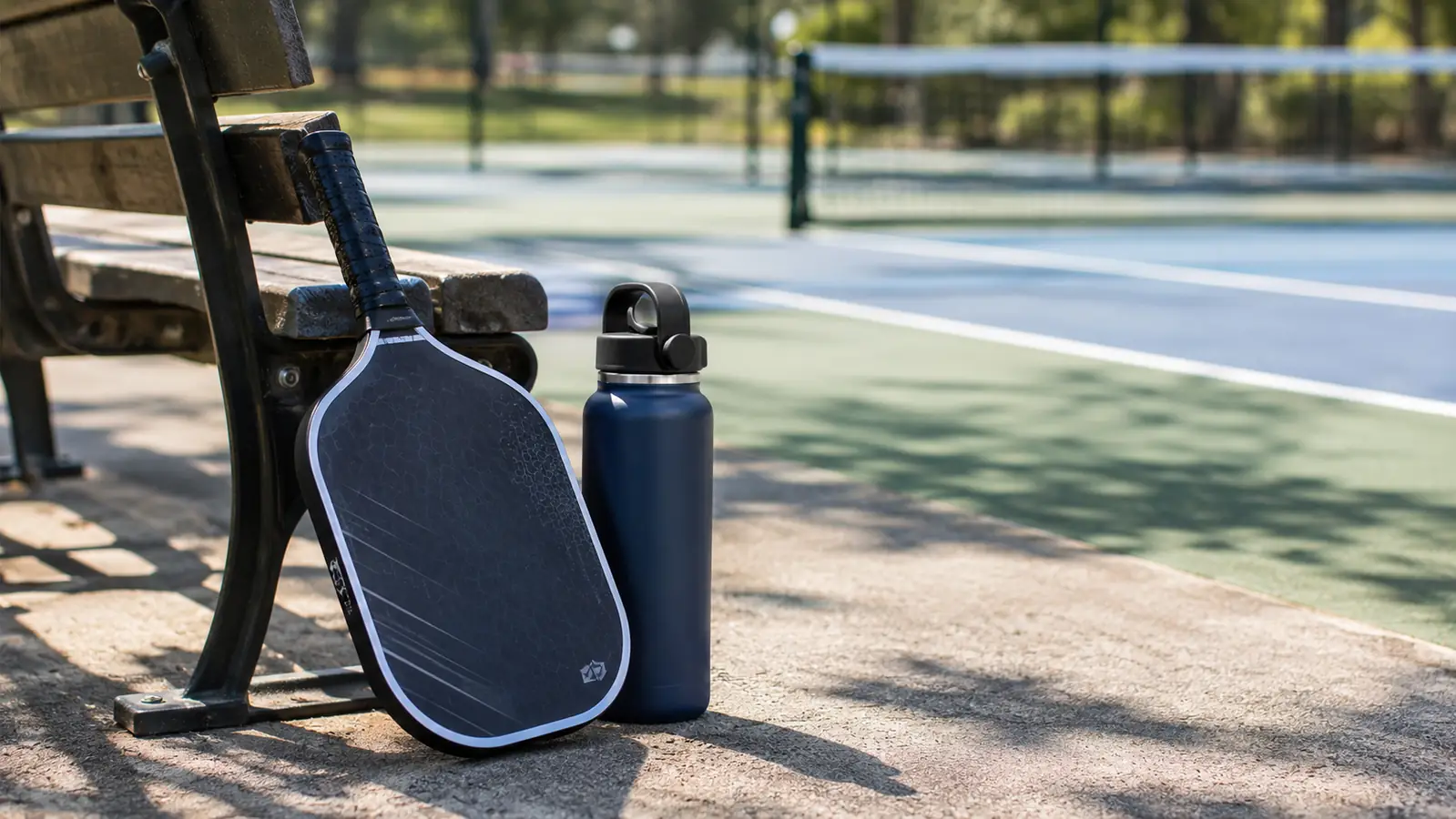 A pickleball paddle leaning against a park bench with a water bottle between games